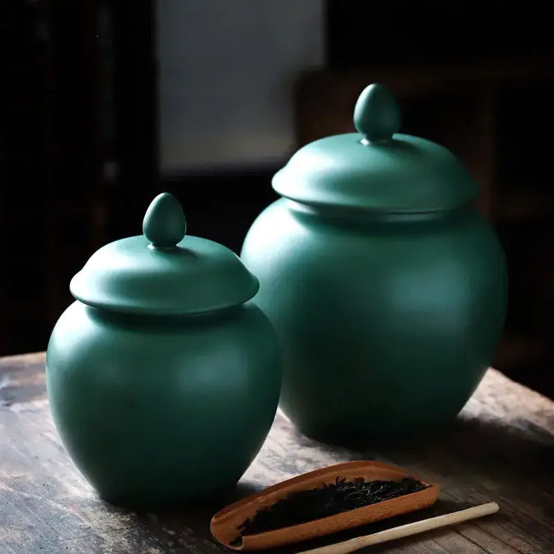 Two matte-finished green ceramic tea caddy jars with rounded bodies and matching lids for kitchen storage