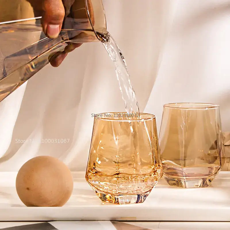 A translucent amber diamond crystal glass water pitcher pouring water into a matching faceted crystal glass cup
