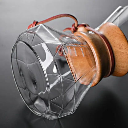 Clear glass hand brew coffee dripper with diamond glass hand design and wooden lid secured by brown leather straps for kitchen use
