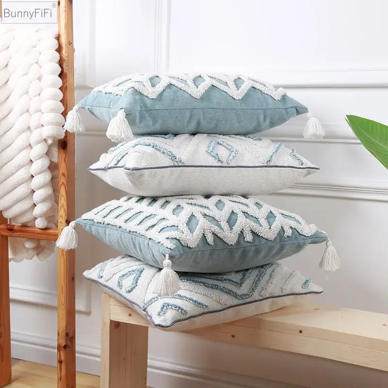Stack of four diamond tufted blue and white cushion covers with embroidered details and tassel accents for living room use