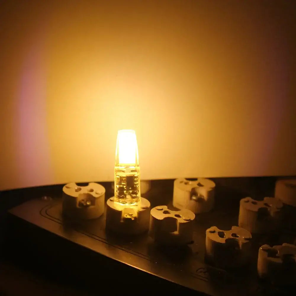 A glowing amber dimmable g4 led bulb with clear glass and metallic base on beige ceramic insulators for living room lighting solution