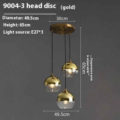 Gold pendant light with three glass globe shades and a brass disc, modern design.
