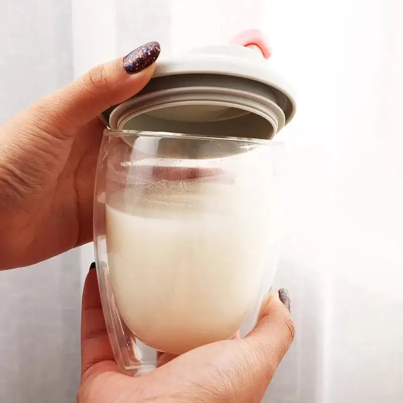 A clear double deck insulated glass mug with a light gray silicone lid and pink handle filled with milk