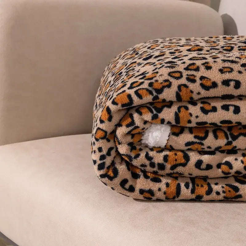 A double layer leopard print coral fleece blanket in cream with bold orange and black pattern for bedroom use