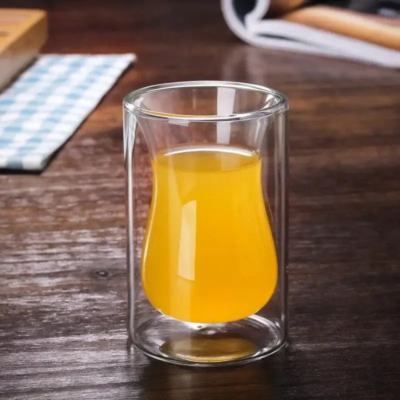 A clear double walled glass mug filled with golden orange liquid from the drinkware collection for dining room use