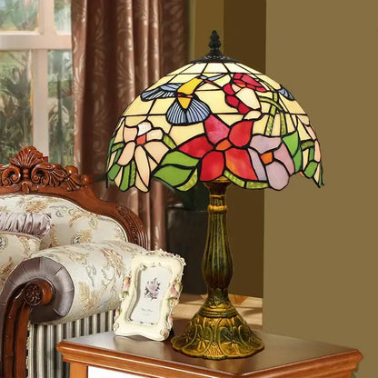 A decorbites dragonfly tiffany stained glass table lamp with multicolored floral and hummingbird panels on a brass base