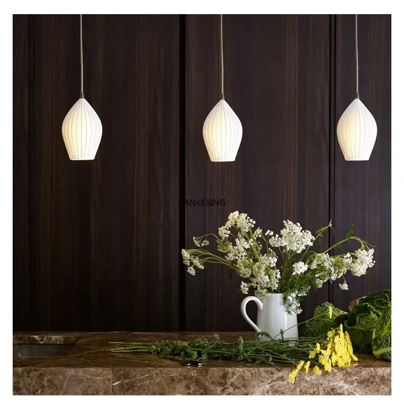 Three elegant white and gold ribbed ceramic pendant lights with teardrop shades hanging in a modern dining room