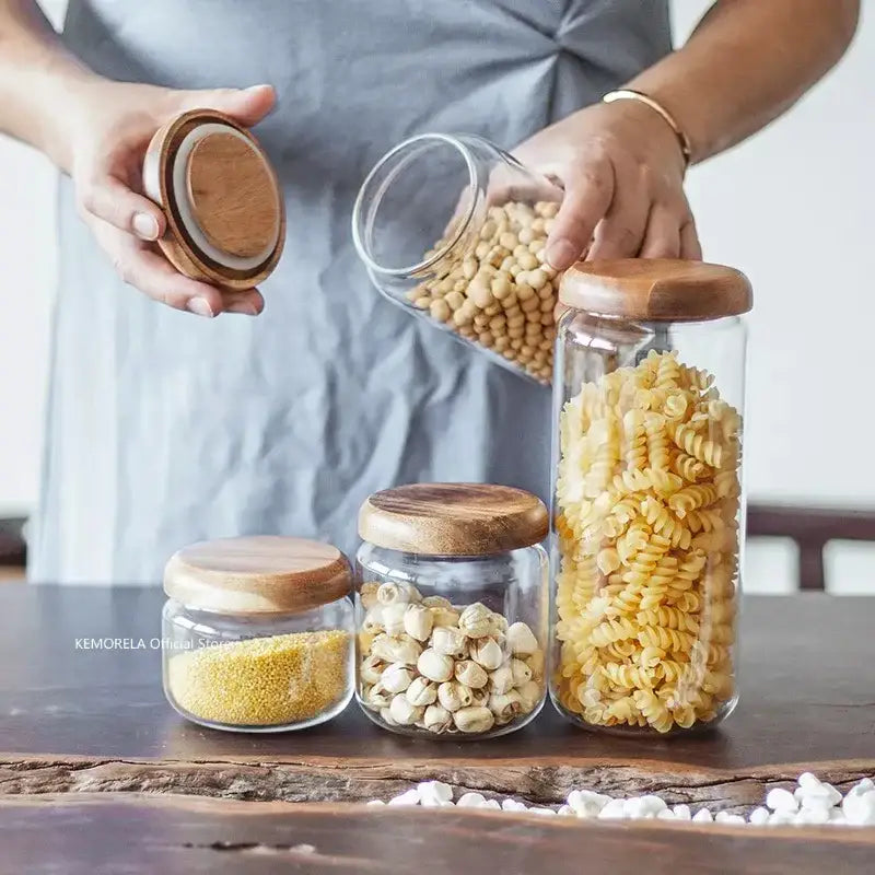 Clear glass storage jars with elegant acacia wood lids holding pasta and grains in kitchen set with wood lid design