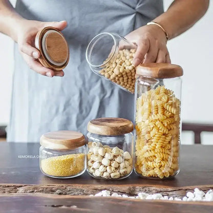 Clear glass storage jars with elegant acacia wood lids holding pasta and grains in kitchen set with wood lid design