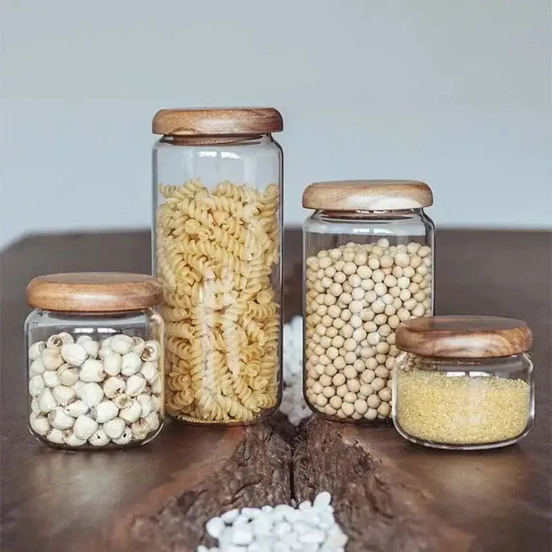 Set of four clear glass food storage jars with natural acacia wood lids holding different dry goods