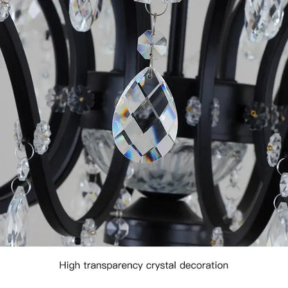 A teardrop-shaped transparent crystal pendant with faceted surfaces on a black metal crystal candle chandelier