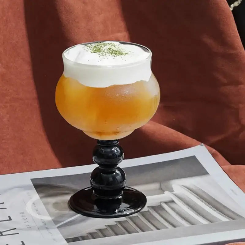 Elegant black goblet glass coffee cup filled with amber beverage topped with white foam and green matcha powder garnish