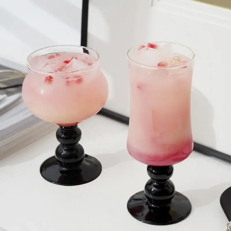 Two elegant black-stemmed goblet glass coffee cups filled with pink beverage and ice cubes for dining room use