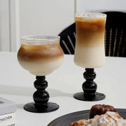Two elegant black goblet glass coffee cups with bulbous stems filled with layered iced coffee for dining room use