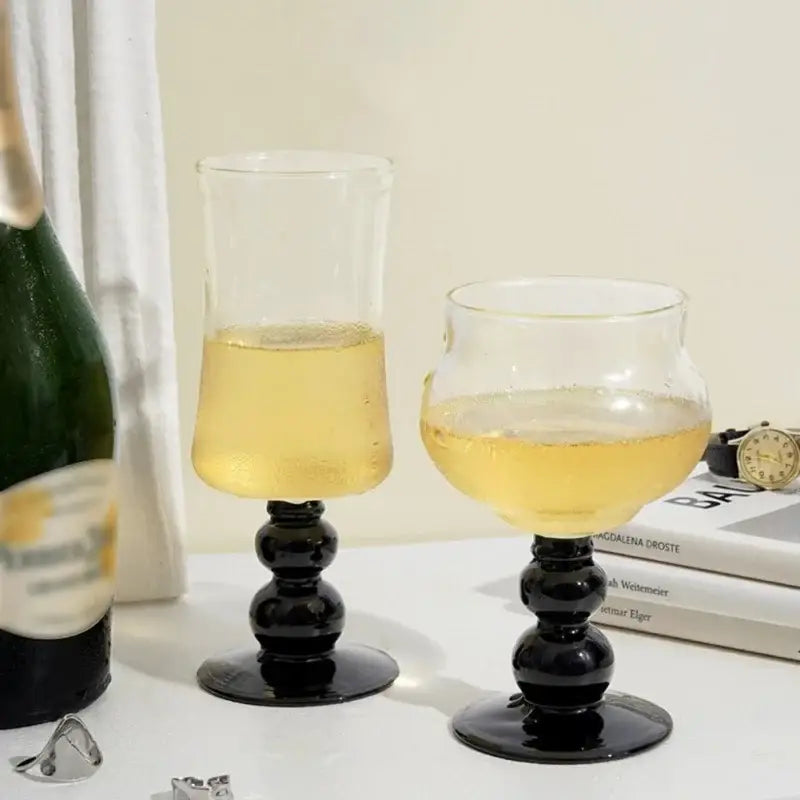 Two elegant black-stemmed goblet glass coffee cups filled with golden sparkling liquid beside a champagne bottle