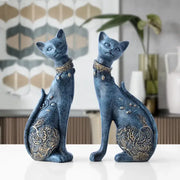 Two elegant blue and gold decorbites cat statues with intricate patterns sitting side by side on a white surface