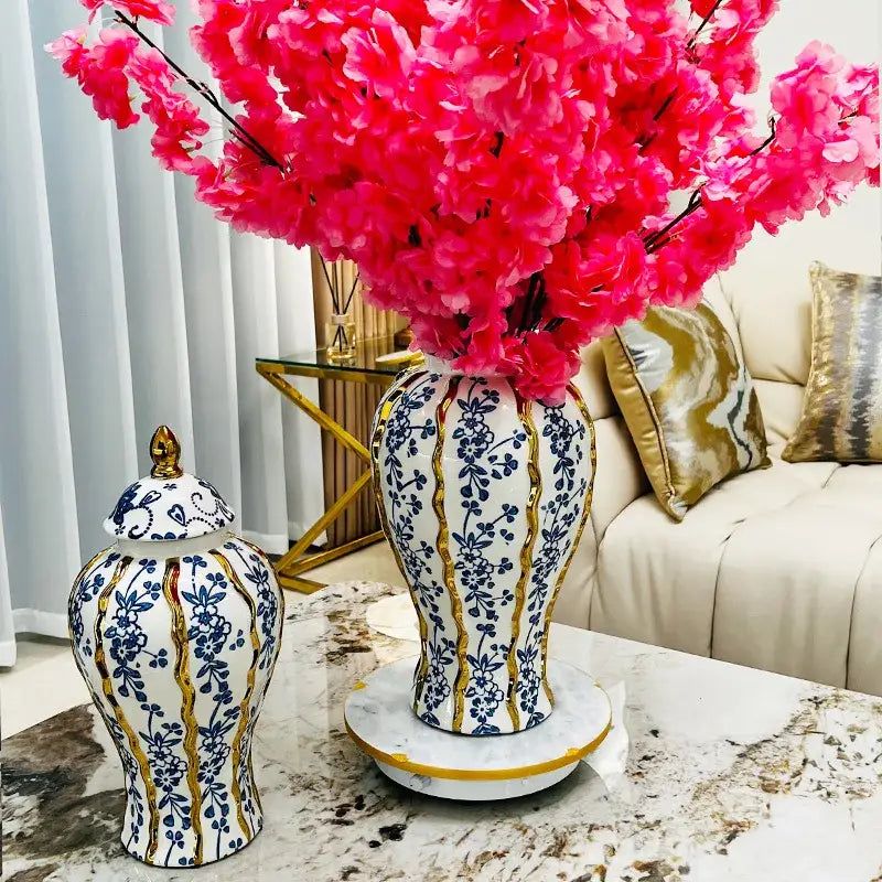 Elegant blue glazed ceramic ginger jar vase with white base, blue floral patterns, gold stripes, and pink artificial blossoms
