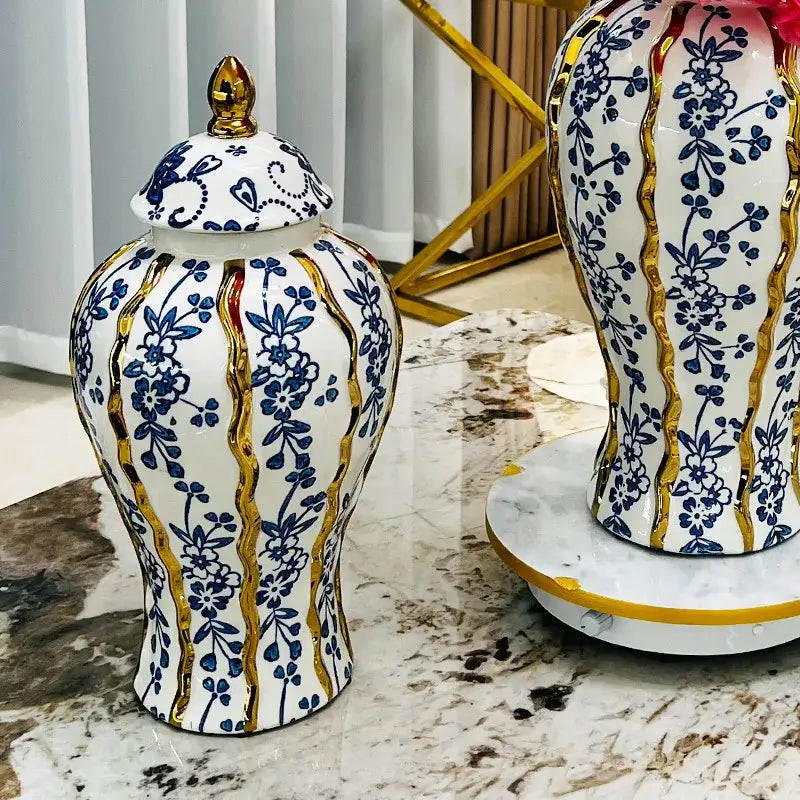 Elegant blue glazed ceramic ginger jar with white base, blue floral patterns, gold trim, and matching lid with golden finial