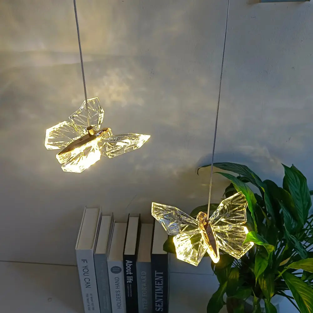 Two illuminated gold-toned decorbites crystal butterfly pendant lamps with faceted wings for bedroom luxury lighting