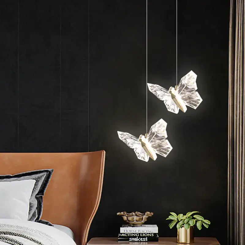 Two translucent crystal butterfly pendant lamps with gold-toned bodies hang on cords against a dark wall for bedroom luxury lighting