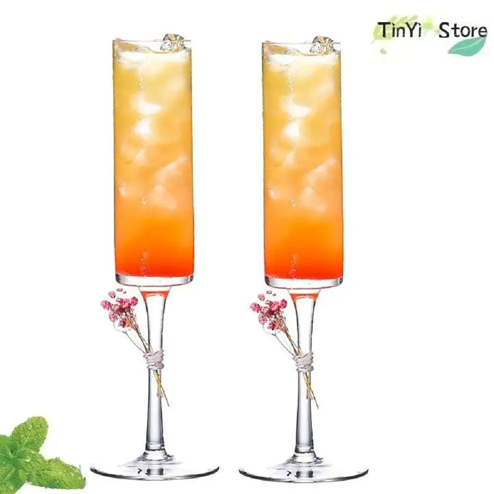 Two elegant clear glass decorbites bubble champagne glasses with orange gradient cocktails and dried flower garnish