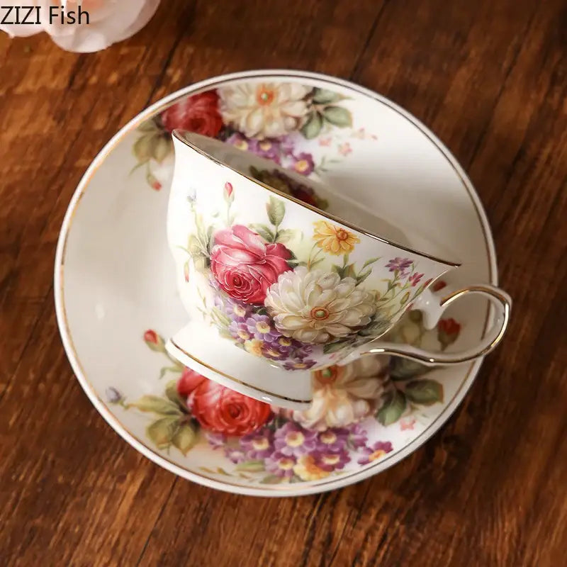 Elegant floral ceramic cup and saucer set with vibrant pink roses purple blossoms and gold trim on creamy porcelain