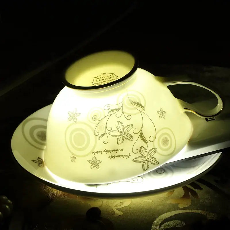 Elegant floral porcelain tea cup set in cream with gold trim and vine patterns resting on a matching saucer