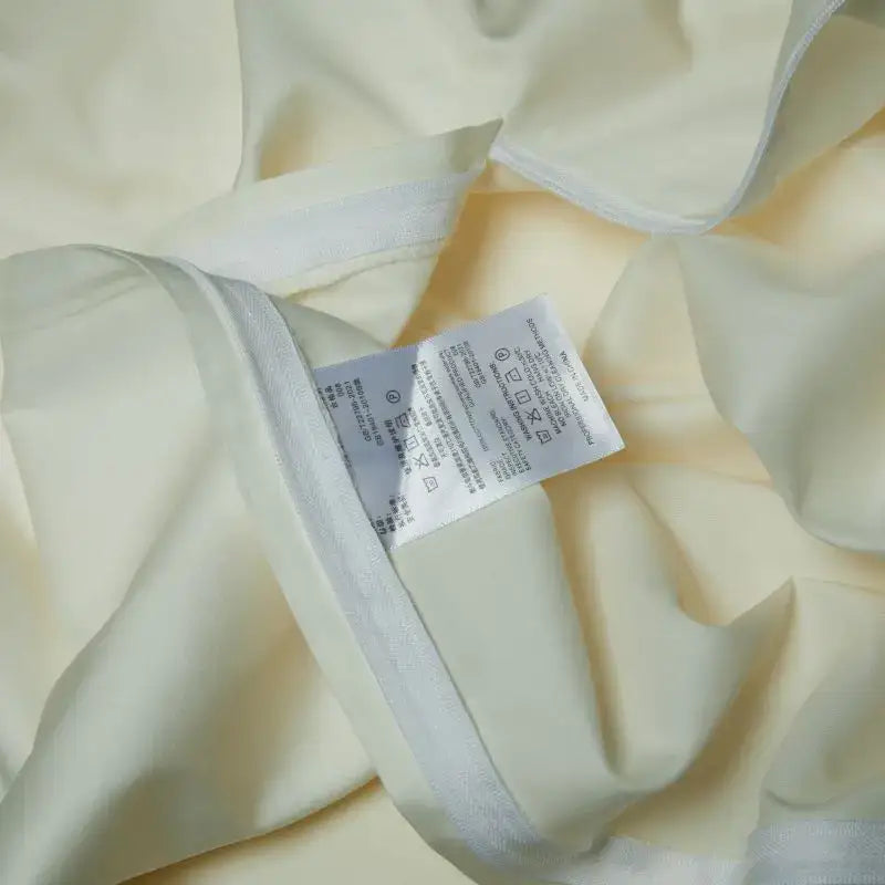 Cream satin bedding set with elegant flowers embroidery and white woven trim featuring a care label in the seam