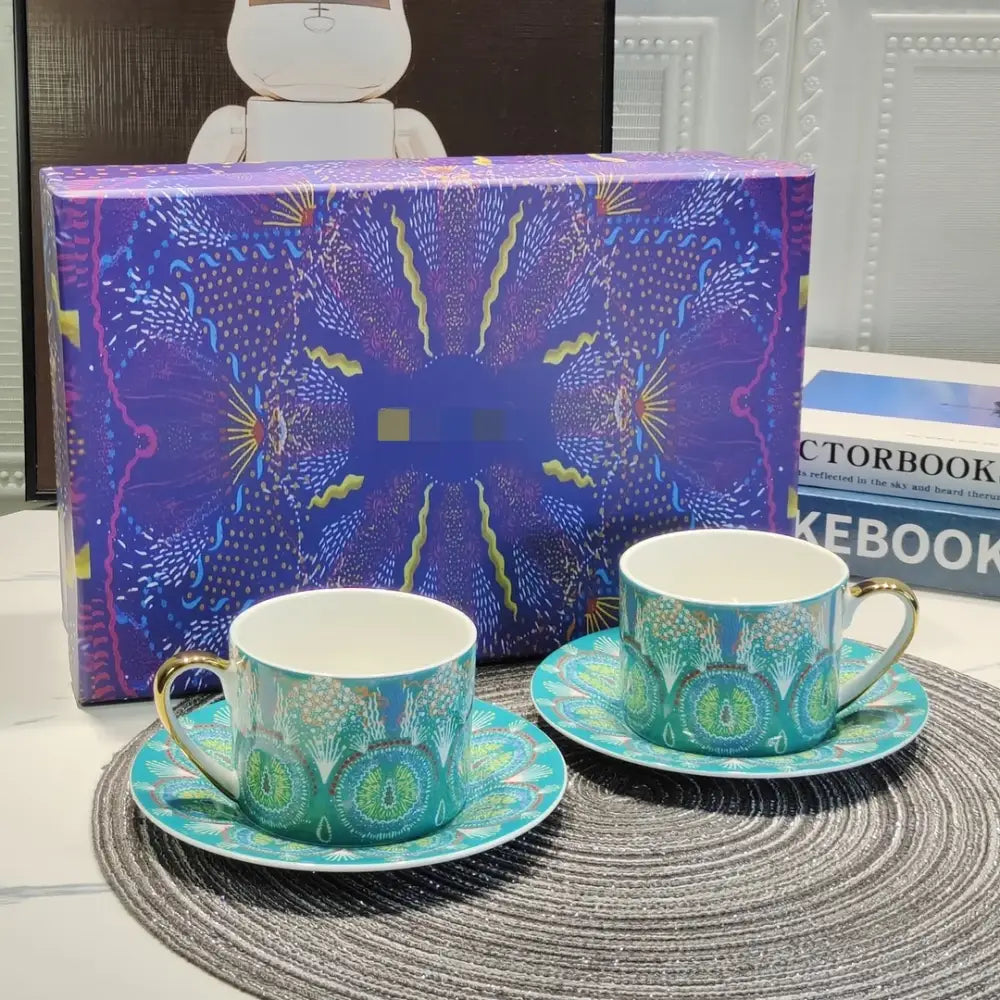 A bone china tea cup set featuring turquoise and green geometric patterns with gold handles on matching saucers