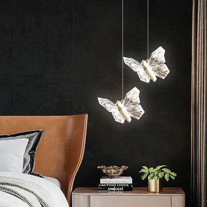 Two translucent crystal butterfly ladder pendant lights with gold centers hanging against a dark wall decorbites butterfly ladder