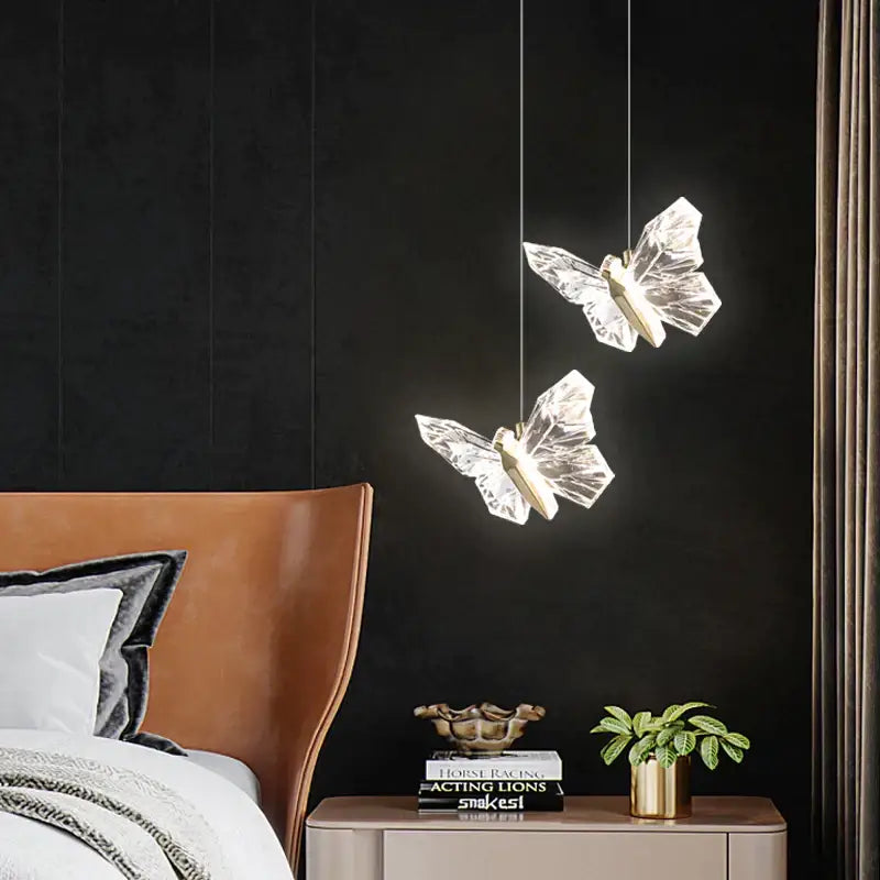 Two translucent crystal butterfly ladder pendant lights with gold centers hanging against a dark wall decorbites butterfly ladder