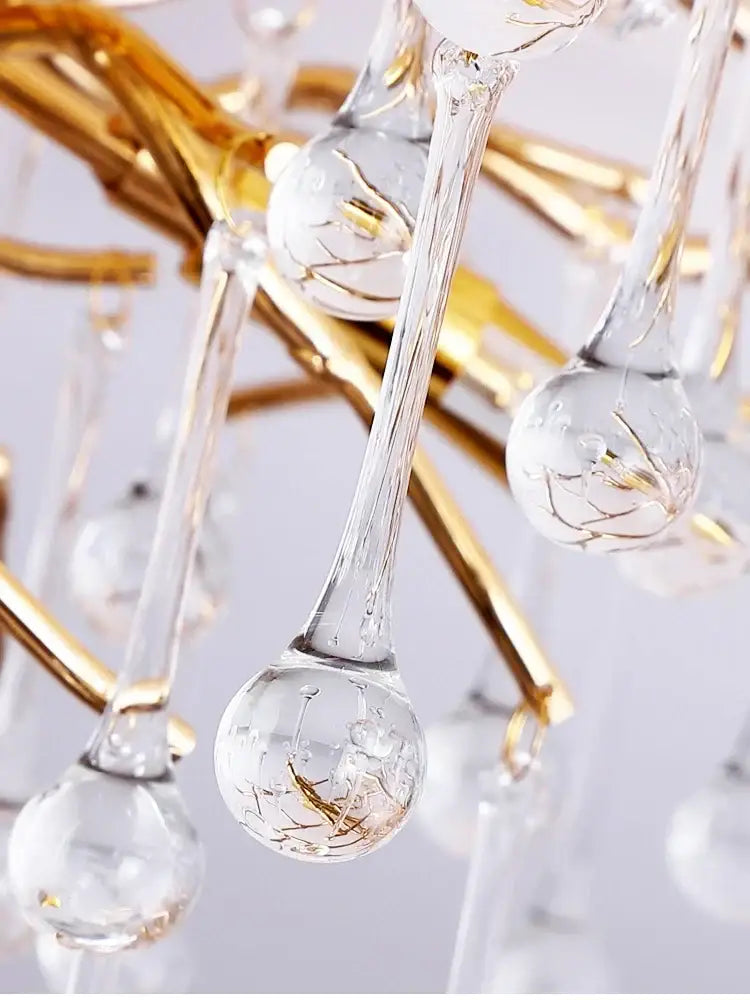 Clear glass teardrop pendants with gold leaf etchings hang from a gold crystal chandelier by decorbites elegant gold