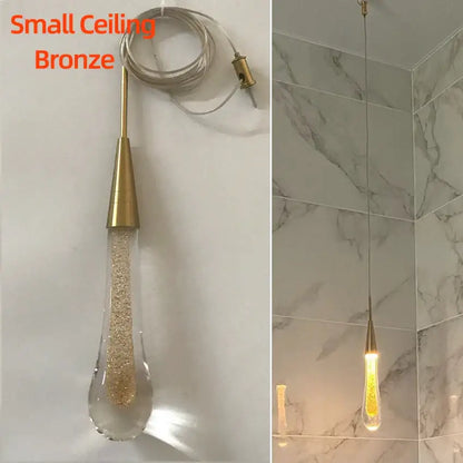 A small bronze pendant light with a teardrop crystal glass led shade filled with golden glitter for dining room decor