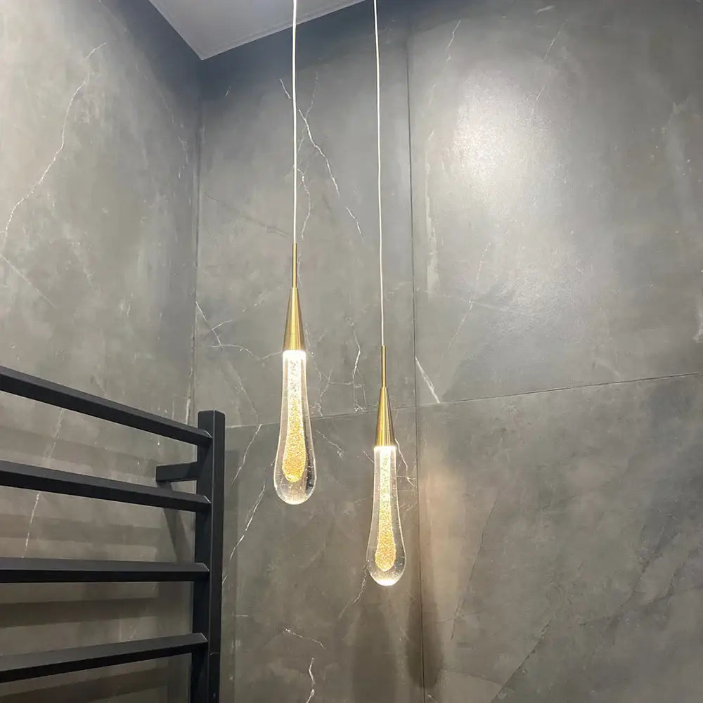 Two elegant gold-toned decorbites crystal glass led pendant lights with teardrop glass shades filled with golden glitter hang