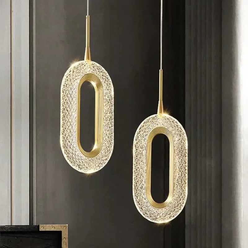 Two elegant gold crystal oval pendant light chandeliers with textured outer shell and illuminated inner frame for living room