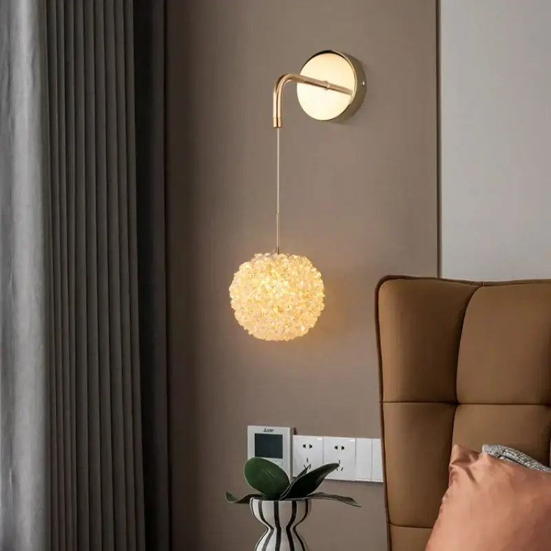 Elegant gold crystal wall lamp with spherical crystal-encrusted shade hanging from curved arm for bedroom decorbites lighting