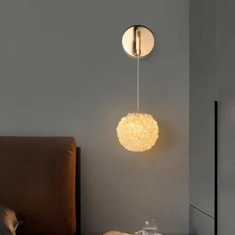 An elegant gold decorbites crystal wall lamp with a warm glowing spherical textured glass shade for bedroom decor