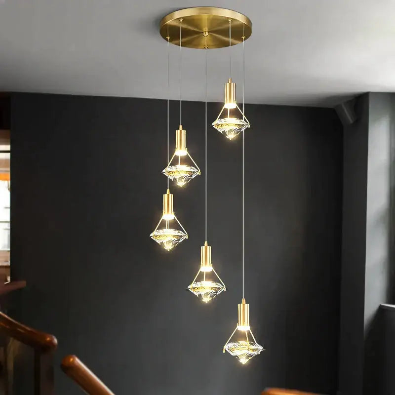 Five elegant gold diamond crystal pendant lights with faceted shades hang from a brass ceiling fixture for dining room