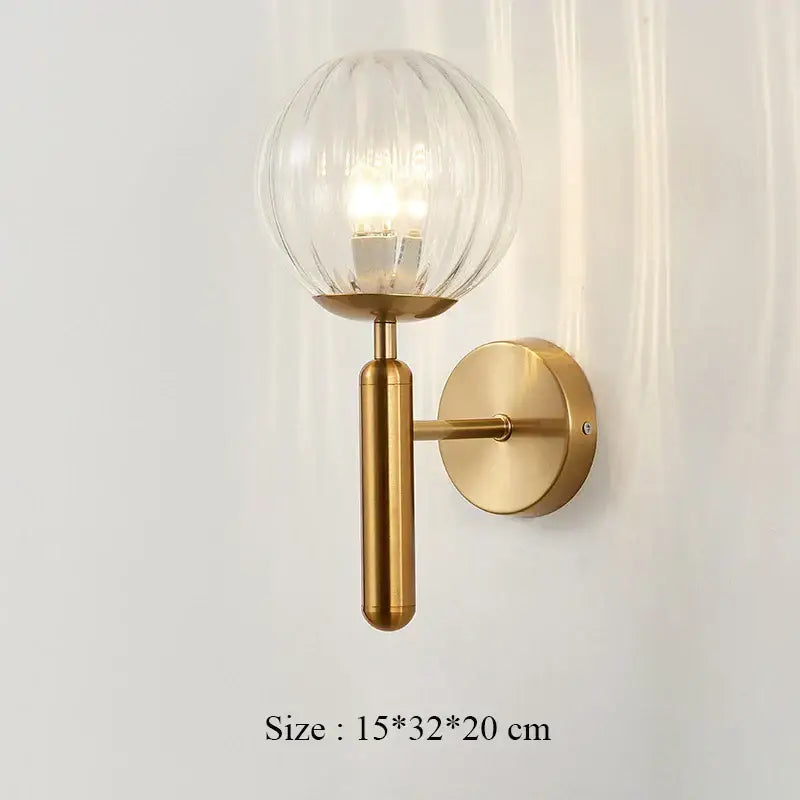 A modern brass decorbites iron wall lamp with ribbed frosted glass globe and cylindrical stem for bedroom decor