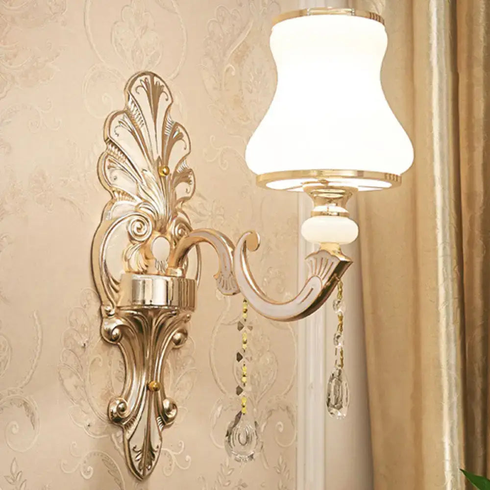 Elegant gold scrolled arm wall mount sconce with ornate gold tone, white frosted glass shade, and crystal beads