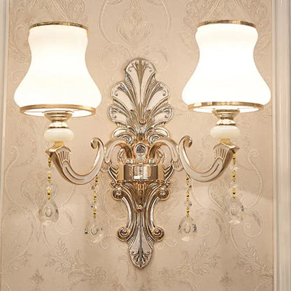 Elegant gold scrolled arm wall mount sconce with two white lampshades and crystal droplets for bedroom lighting
