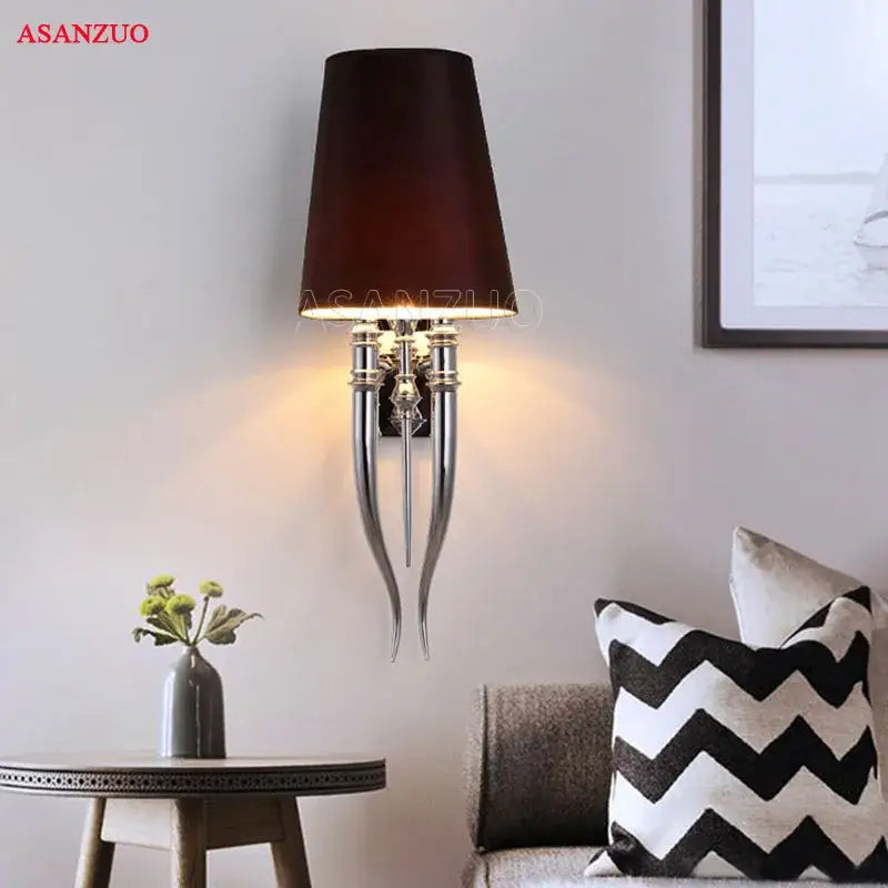 Dark brown lampshade on chrome iron claw horn wall sconce with three curved arms for elegant bedroom lighting