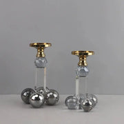 A pair of elegant clear crystal geometric candle holders with gray spheres and gold-toned tops on acrylic bases