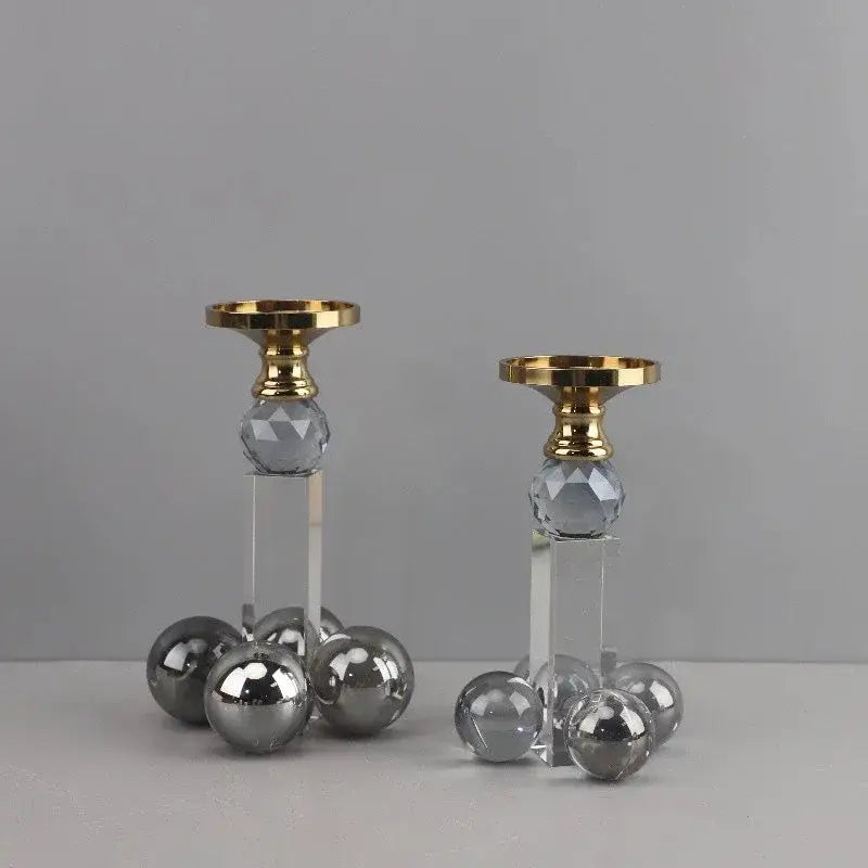 A pair of elegant clear crystal geometric candle holders with gray spheres and gold-toned tops on acrylic bases