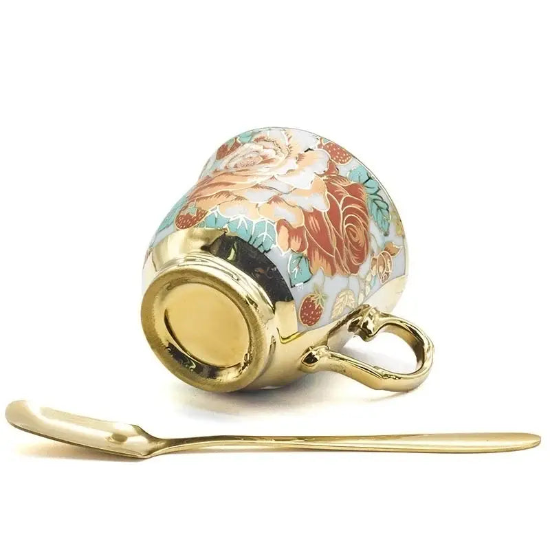 A delicate porcelain coffee cup with hand painted flower floral patterns in warm orange and teal hues and gold rim