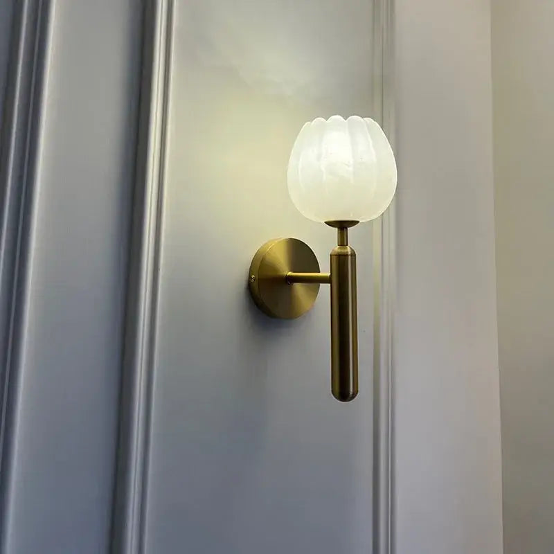 Delicate brass wall lamp with frosted white petal glass shade and marble wall accent for elegant bedroom decor
