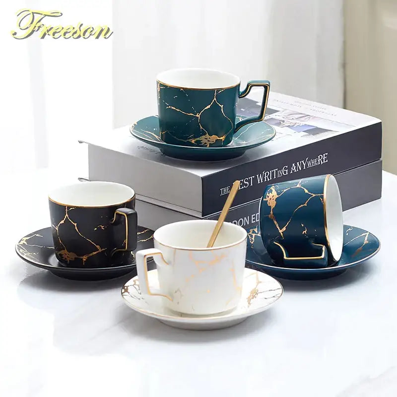 Set of four elegant ceramic tea set cups and saucers in black, deep teal, and white with gold marble pattern