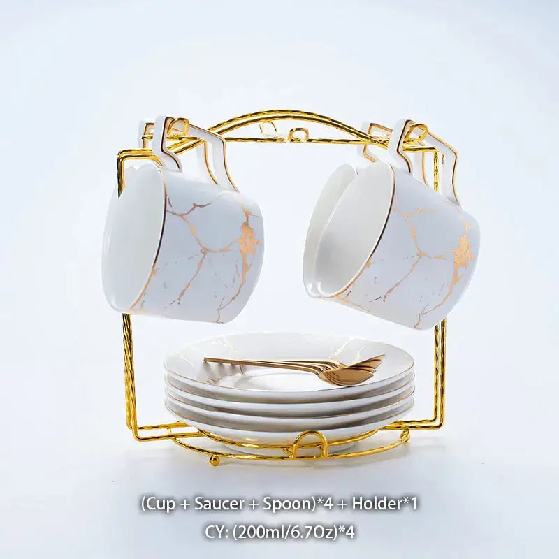 Elegant marble ceramic tea set featuring white mugs with gold veining and rims on a gold metal rack with saucers and spoons