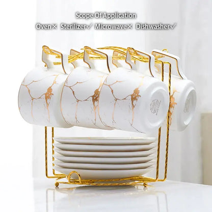 Elegant marble ceramic tea set featuring white mugs with gold marble patterns and handles on a golden rack with plates