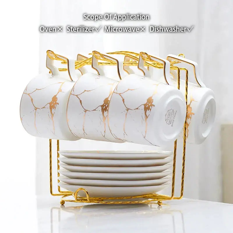Elegant marble ceramic tea set featuring white mugs with gold marble patterns and handles on a golden rack with plates